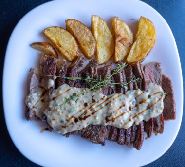 Baharatlı, orta pişmiş biftek, hardal sosu ve patates, beyaz tabak, siyah arka plan.