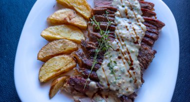Baharatlı, orta pişmiş biftek, hardal sosu ve patates, beyaz tabak, siyah arka plan.