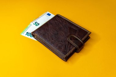 Turuncu arka planda izole edilmiş, içinde banknotlar ve kredi kartı bulunan kahverengi, hakiki deri cüzdanın üst görüntüsü.