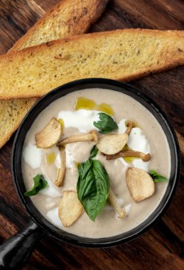 Ahşap tahtada siyah seramik kasede mantar çorbası.