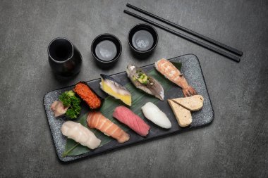 Japon restoranındaki gri arka planda saki ile karışık suşi seti.