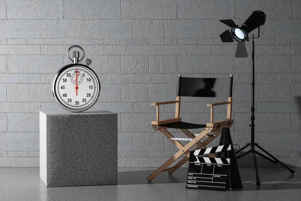 Stopwatch with Blank Screen near Director Chair, Movie Clapper and Spotlight in front of stone blocks wall background. 3d Rendering