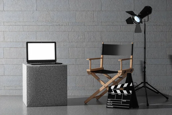 石のブロックの壁の背景の前に監督の椅子 映画のクラッパーとスポットライトの近くにブランクスクリーンと現代のラップトップ 3Dレンダリング — ストック写真