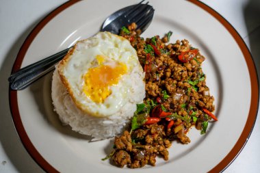 Stir fried Thai basil with minced pork and a fried egg on white plate