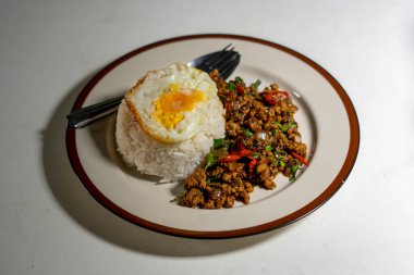 Stir fried Thai basil with minced pork and a fried egg on white plate