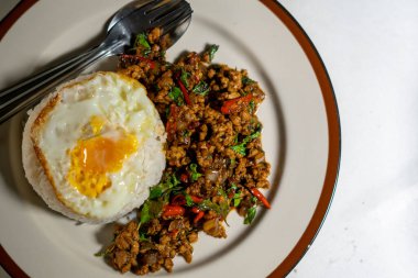Stir fried Thai basil with minced pork and a fried egg on white plate