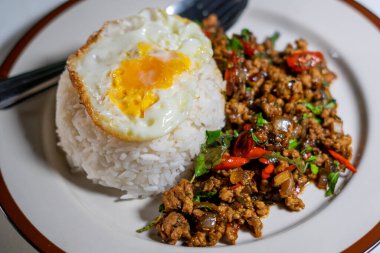 Stir fried Thai basil with minced pork and a fried egg on white plate