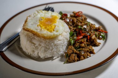Stir fried Thai basil with minced pork and a fried egg on white plate