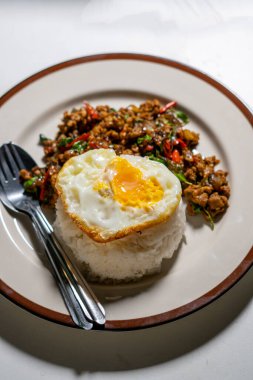 Stir fried Thai basil with minced pork and a fried egg on white plate