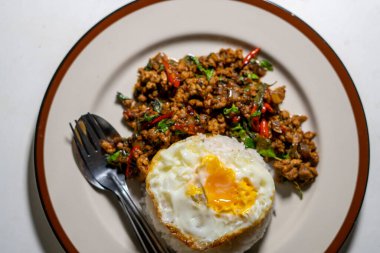 Stir fried Thai basil with minced pork and a fried egg on white plate