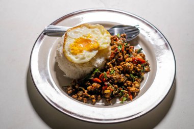 Stir fried Thai basil with minced pork and a fried egg on white plate