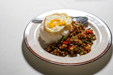 Stir fried Thai basil with minced pork and a fried egg on white plate