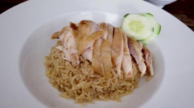 Dilimlenmiş Hainan usulü tavuk ve terbiye edilmiş pirinç, acı biber sosu ve beyaz tabakta salatalık.