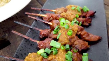 Dilimlenmiş Hainan usulü tavuk ve terbiye edilmiş pirinç, acı biber sosu ve beyaz tabakta salatalık.