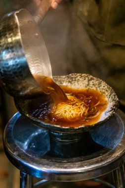 Sapporo ramen eriştesi siyah arka planda buharlı kırmızı çubuklarla kaldırıldı.