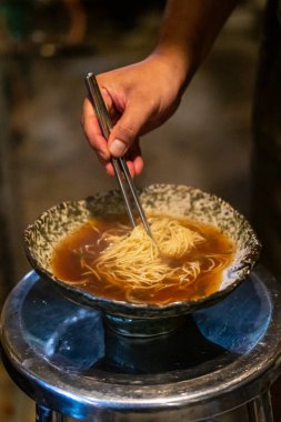 Sapporo ramen eriştesi siyah arka planda buharlı kırmızı çubuklarla kaldırıldı.