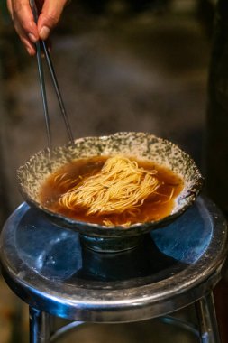 Sapporo ramen eriştesi siyah arka planda buharlı kırmızı çubuklarla kaldırıldı.