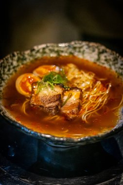 Sapporo ramen eriştesi siyah arka planda buharlı kırmızı çubuklarla kaldırıldı.