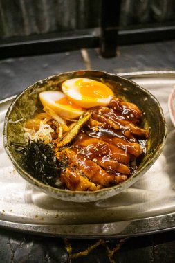 Bir kase teriyaki tavuğunun yüksek açılı yakın plan görüntüsü. Seramik ya da toprak kaplama gibi görünen kase, soluk, gri-yeşil tonlarda ince varyasyonlu bir renktir..