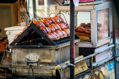Beyaz tabakta geleneksel Tayland sosisi. Biraz ekşi ve tuzlu, genellikle ızgara ya da kızarmış, yanında çiğ biber, taze zencefil dilimleri, sarımsak ve taze sebzelerle servis edilir.