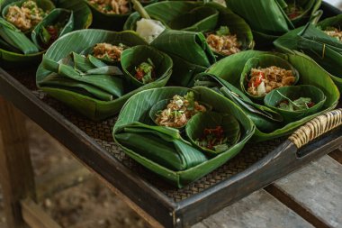 Geleneksel Tayland yemeklerini eko-dost muz yaprağı kaplarında sunan güzel bir resim. Her porsiyon dilimlenmiş et, otlar ve kırmızı biber karışımı içeriyor., 