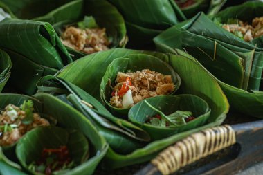 Geleneksel Tayland yemeklerini eko-dost muz yaprağı kaplarında sunan güzel bir resim. Her porsiyon dilimlenmiş et, otlar ve kırmızı biber karışımı içeriyor., 
