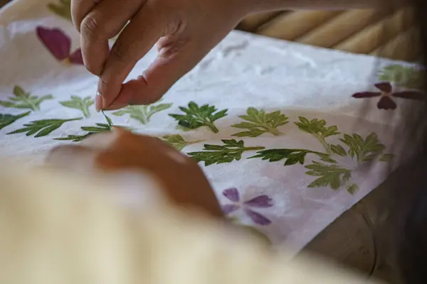 Eller kumaş üzerinde doğal yaprak izleri yaratıyor. Çekiç teknikleri kullanıyor. Çevre dostu ve yaratıcı zanaat süreci..