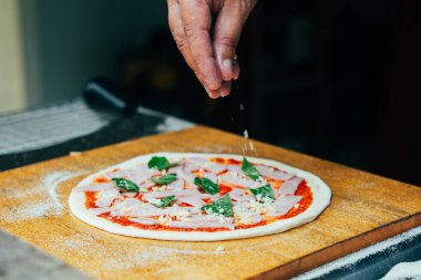 Jambon ve domates soslu taze fesleğene taze fesleğen yaprağı ekleyin. Ev yapımı pizza yapma sürecinde ahşap pizza kabuğuna yakalanan bir adım..