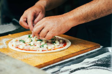 Jambon ve domates soslu taze fesleğene taze fesleğen yaprağı ekleyin. Ev yapımı pizza yapma sürecinde ahşap pizza kabuğuna yakalanan bir adım..