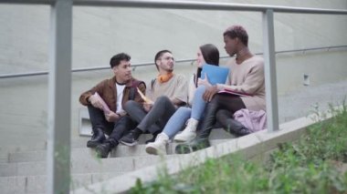 Çok ırklı bir grup öğrenci, üniversite kampüsünün merdivenlerinde oturuyorlar..