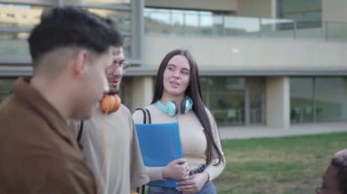 Bir grup kadın ve erkek büyük pencereli bir binanın önünde konuşuyorlar. Orta boy..