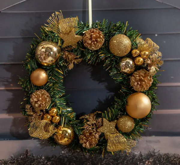 Christmas wreath against white wooden wall with golden ornaments, Christmas balls, festive holiday background. A Beautiful Christmas holiday wreath of gold  hangs on a wall.