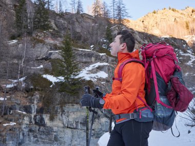 Popüler kış aktiviteleri. Sırt çantasıyla yürüyüş yapan erkek yürüyüşçü ve karda yürüyen sırıklar..