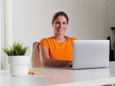 Evde dizüstü bilgisayarla çalışan gülümseyen kadın.