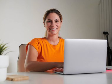 Evde dizüstü bilgisayarla çalışan gülümseyen kadın.