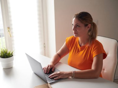 Evde dizüstü bilgisayarla çalışan gülümseyen kadın.