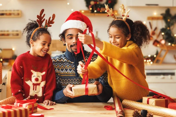 Happy african american family father and kids daughter and son pack Christmas gifts