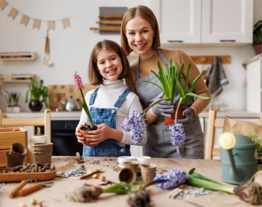 Mutlu anne ve çocuk gündelik giysiler içinde sümbül çiçekleriyle gülümsüyor ve kameraya bakıyor. Masanın arkasında duruyor ve mutfakta bahçeyle uğraşıyor.