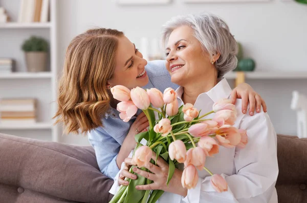 Positive elegant elderly woman with bunch of fresh tulips smiling and accepts a gift from a young daughter during a mothers day celebration