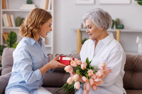 在母亲节的庆祝活动中 一位积极优雅的老妇人带着一束新鲜的郁金香微笑着接受着一个小女孩的礼物 — 图库照片