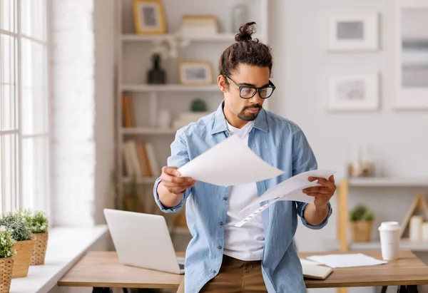 stock image Pensive African American male freelancer in glasses reading papers and working on business project while standing at table in workspace