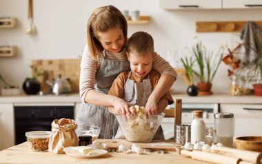 Neşeli aile: Anne ve önlüklü çocuk birlikte fırın pişirirken mutfaktaki ahşap masada pasta yapıyorlar.