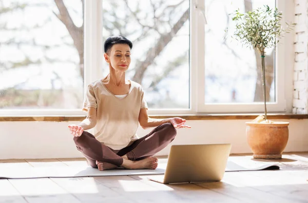 中年妇女赤脚活动时穿着紧闭的眼睛和荷花中的冥想姿势在网上瑜伽课的窗口 在家里的早晨 — 图库照片