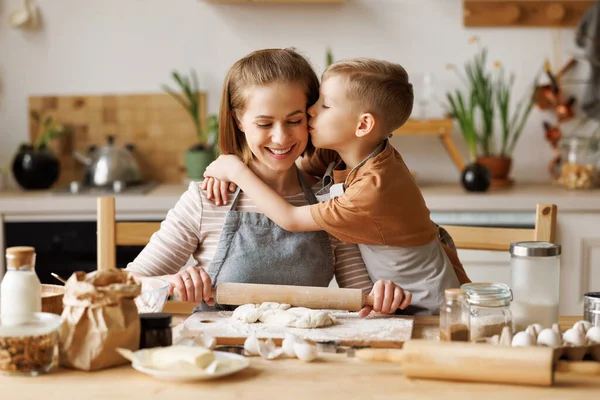 stock image Cute son embracing and kissing mother rolling dough at wooden table while preparing bakery in kitchen 