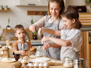 Tatmin edici anne ve tatlı çocuklar: Oğul ve kız kaseye malzeme ekliyor ve evde hamur hazırlıyorlar.