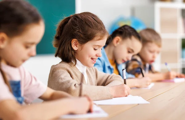 Pozitív Kis Diák Mosolyog Írja Adatokat Noteszbe Miközben Asztalnál Közelében — Stock Fotó