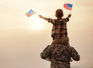 Amerikan bayrağını omuzlarında taşıyan ve güneşli bir günde harika yaz manzarasının tadını çıkaran mutlu bir baba, mutlu bir erkek asker, Amerikan ordusundan sonra oğluyla bir araya geldi.