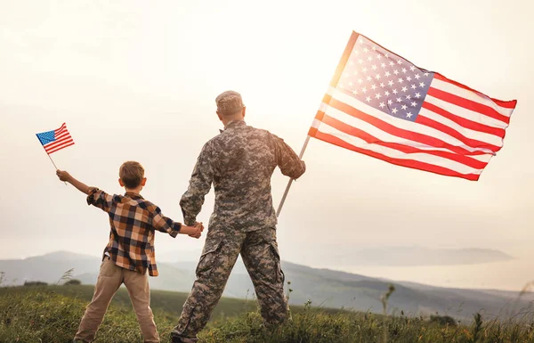Rear view of military man father holding   son's hand   with american flag   and enjoying amazing summer nature view on sunny day, happy male soldier dad reunited with son after US army