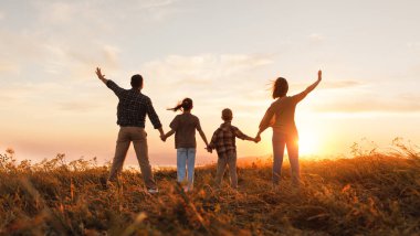 Mutlu aile: anne, baba, çocuk, oğul ve kız gün batımında doğanın arkasında durur.