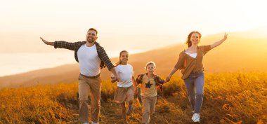 Mutlu aile: anne, baba, çocuklar gün batımında doğada koşan oğul ve kız